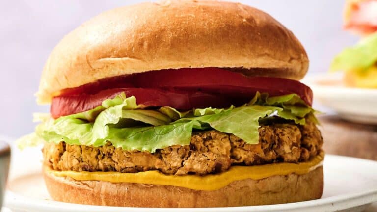 A veggie burger topped with lettuce, tomato slices, and mustard in a sandwich bun, served on a white plate.