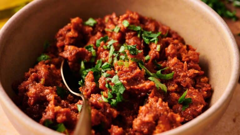 A bowl of seasoned ground meat garnished with chopped fresh herbs, with a spoon resting inside.