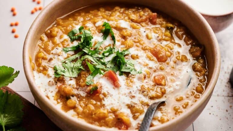 A bowl of lentil curry garnished with chopped cilantro and a swirl of cream, with a spoon inside the bowl.