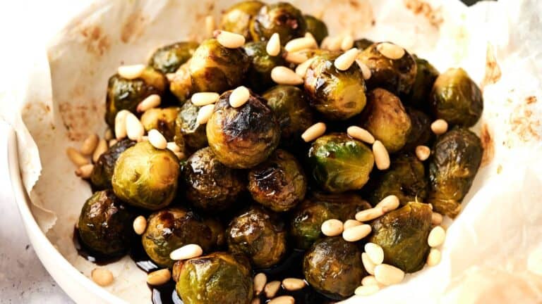 A plate of roasted Brussels sprouts topped with pine nuts on parchment paper.