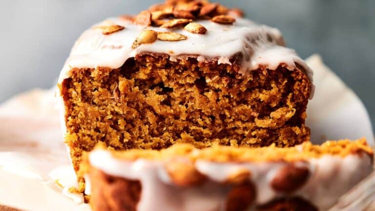 A close-up of a sliced pumpkin bread loaf topped with white icing and pumpkin seeds.