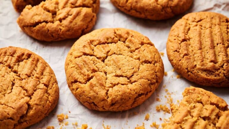 Several peanut butter cookies are arranged on crumpled parchment paper, with visible crumbs surrounding them.