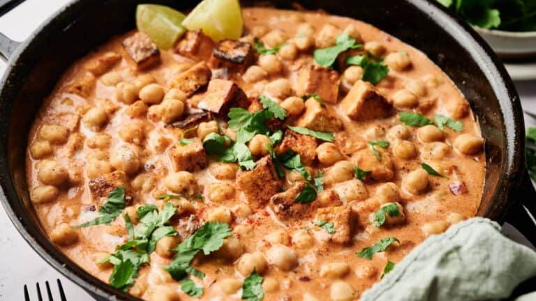 Chickpea and tofu curry in a skillet, garnished with fresh cilantro and lime wedges.