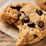 An Air Fryer Vegan Chocolate Chip Cookie with a bite taken out, resting on a piece of parchment paper.