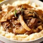 A bowl of mashed potatoes topped with rich vegan mushroom gravy and garnished with fresh rosemary.