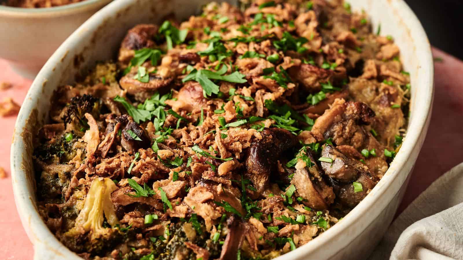 A baked casserole topped with chopped herbs and crispy fried onions, containing pieces of broccoli and mushrooms, served in an oval dish.