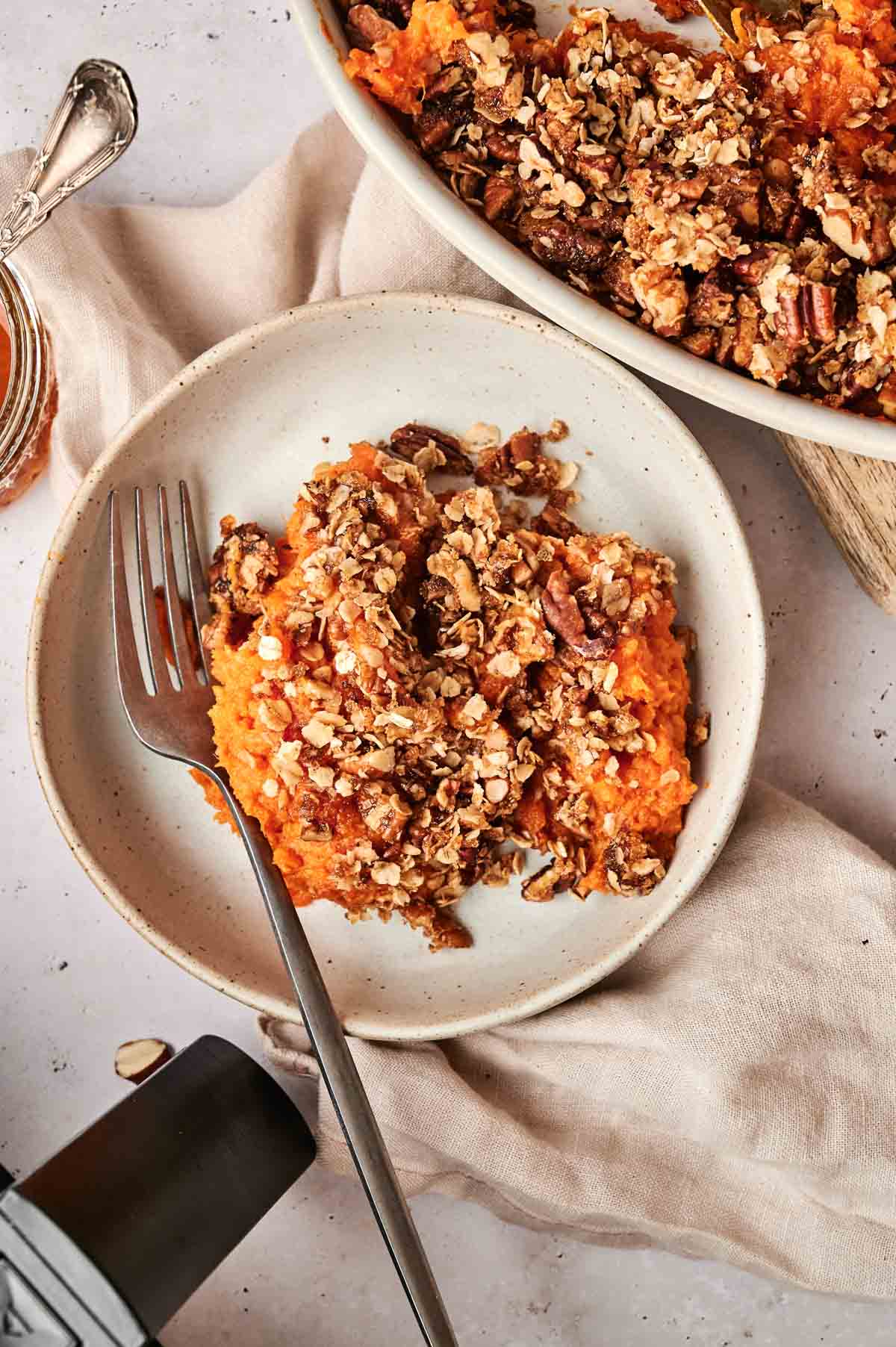 A plate with Air Fryer Sweet Potato Casserole topped with oat and pecan crumble, a fork resting on the side; serving dish visible in the background.