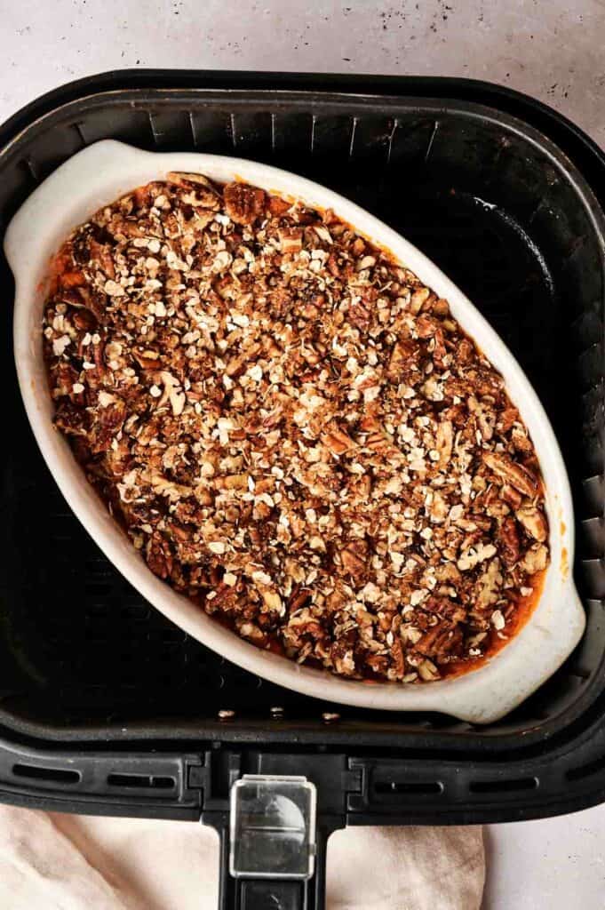 An oval baking dish filled with Air Fryer Sweet Potato Casserole, topped with a pecan and oat crumble, sits inside an air fryer basket.
