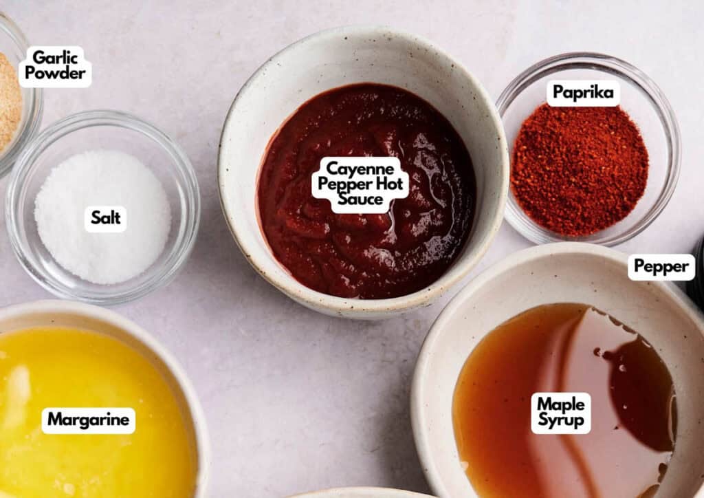 Various labeled ingredients in small bowls on a countertop, including garlic powder, salt, margarine, cayenne pepper hot sauce&mdash;perfect for making Buffalo Sauce&mdash;along with paprika, pepper, and maple syrup.