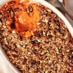 An Air Fryer Sweet Potato Casserole topped with a pecan and oat crumble, with a serving scooped out, in an oval white dish.
