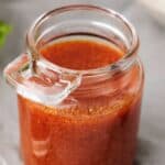 A glass jar filled with reddish-brown Buffalo Sauce sits on a gray surface.