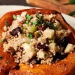 A Stuffed Acorn Squash half filled with a quinoa salad of chopped apples, raisins, nuts, and fresh herbs, served on a white plate.