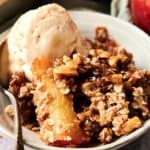 A bowl of Vegan Apple Crisp with a scoop of vanilla ice cream, featuring tender baked apple slices, oat crumble topping, and a spoon.