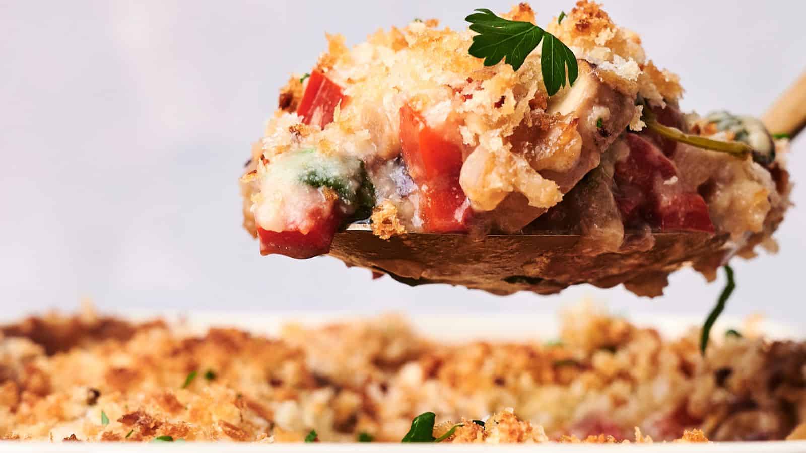 A close-up of a wooden spoon holding a scoop of vegetable casserole topped with golden breadcrumbs, with the casserole dish in the background.A close-up of a wooden spoon holding a scoop of vegetable casserole topped with golden breadcrumbs, with the casserole dish in the background.