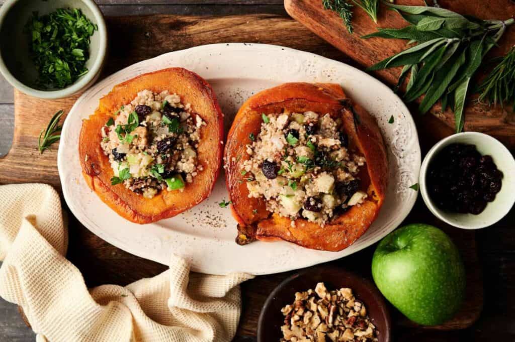 Roasted stuffed acorn squash with vegan stuffing and herbs on a white plate.
