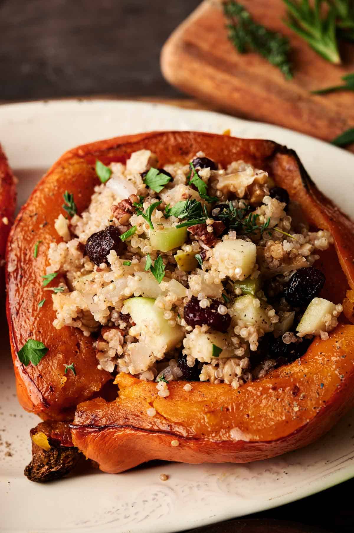 A Stuffed Acorn Squash half brims with couscous, chopped apples, nuts, dried cranberries, and fresh herbs, served beautifully on a white plate.