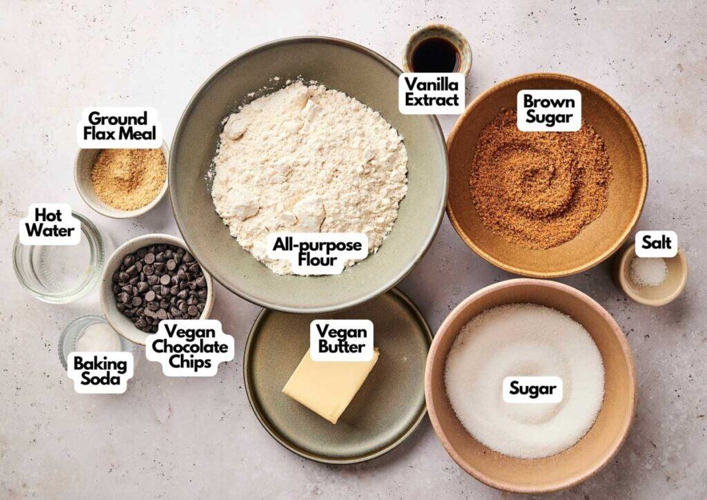 Bowls containing ingredients for Air Fryer Vegan Chocolate Chip Cookies&mdash;flour, brown sugar, vegan butter, chocolate chips, flax meal, and more&mdash;are arranged on a light surface.