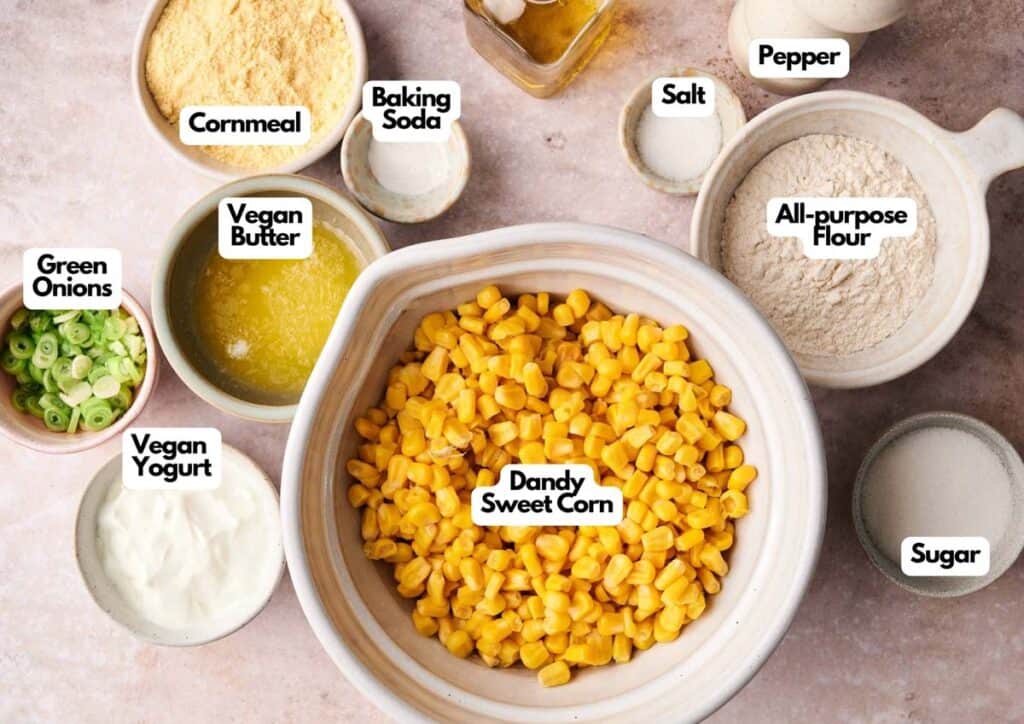 Bowls containing ingredients for Air Fryer Vegan Corn Casserole&mdash;corn, cornmeal, all-purpose flour, baking soda, vegan butter, vegan yogurt, green onions, salt, pepper, and sugar&mdash;are arranged neatly on a countertop.