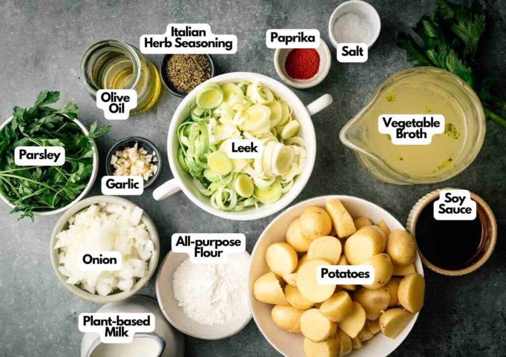 Top-down view of labeled ingredients for Vegan Potato Soup, including potatoes, leek, onion, garlic, parsley, olive oil, flour, plant-based milk, soy sauce, vegetable broth, salt, paprika, and Italian herbs.