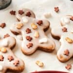 Three Air Fryer Vegan Gingerbread Cookies shaped like people are decorated with small brown and white candy pieces on a sheet of parchment paper.