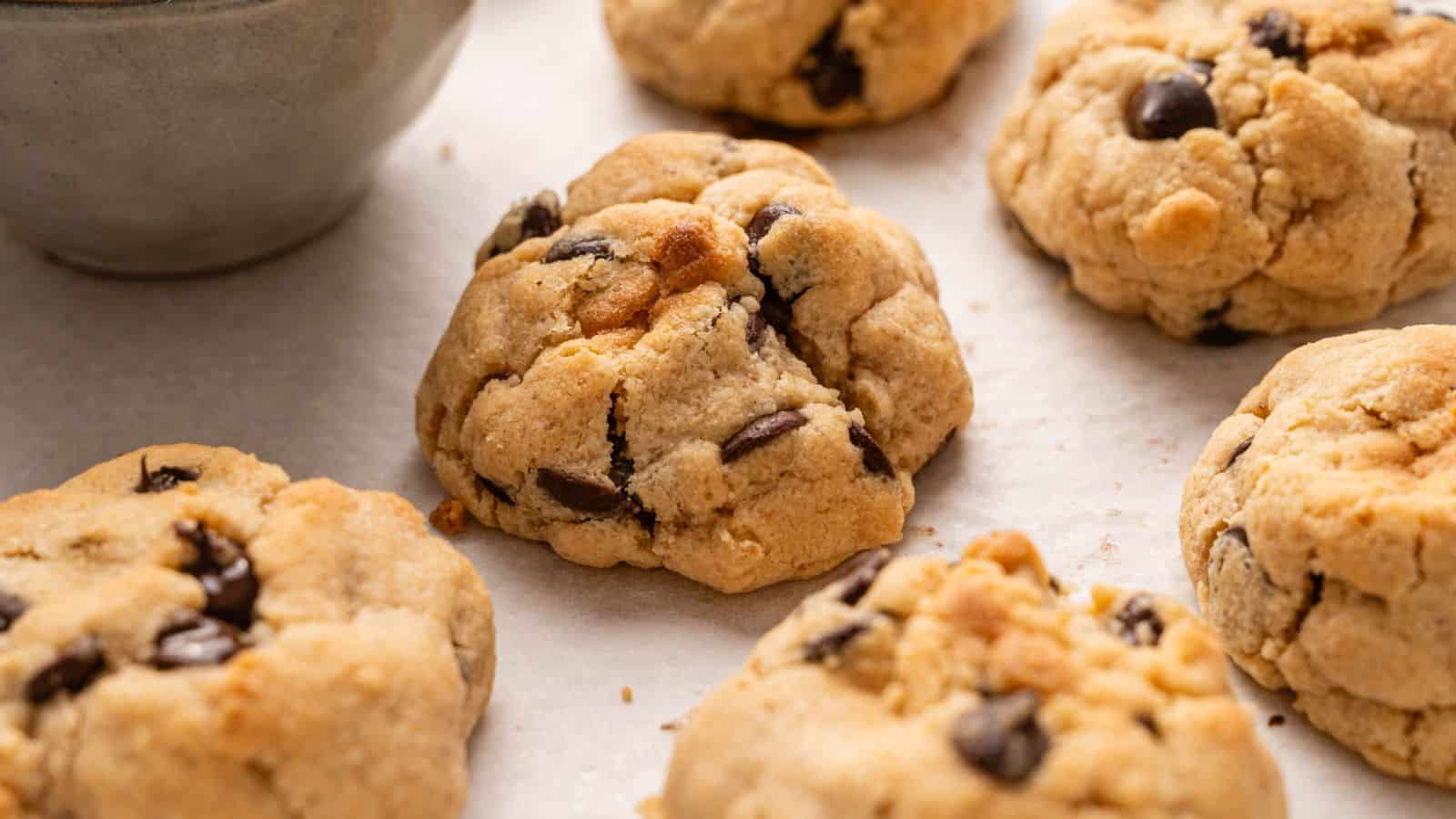 Several chocolate chip cookies on a sheet of parchment paper, with part of a bowl visible in the corner.