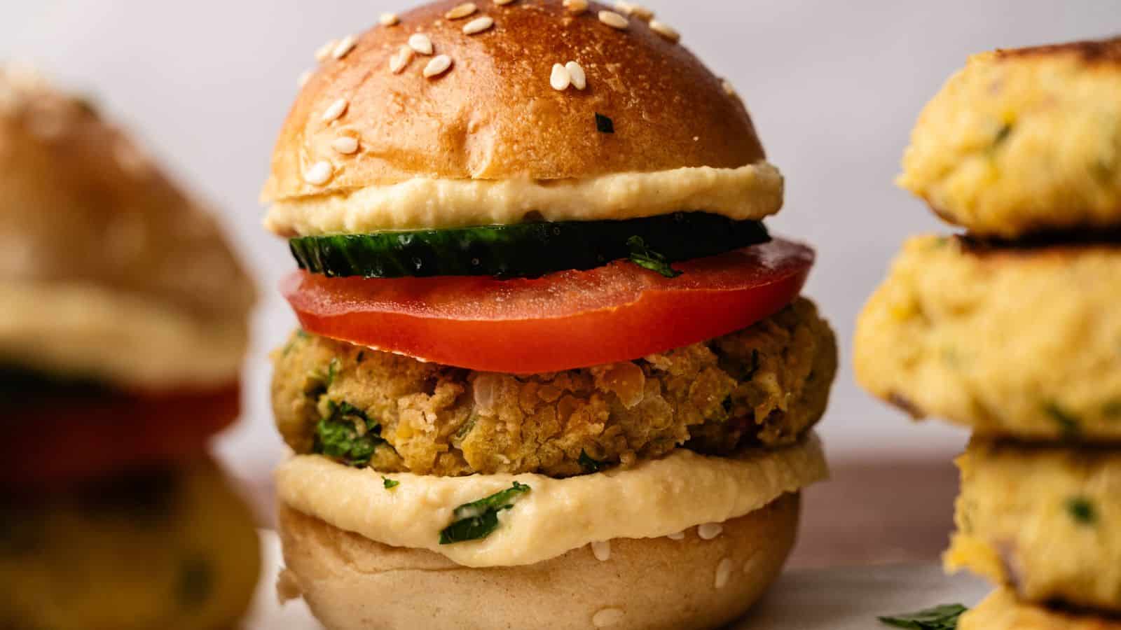 A close-up of a vegetarian falafel slider with tomato, cucumber, and hummus on a sesame bun.