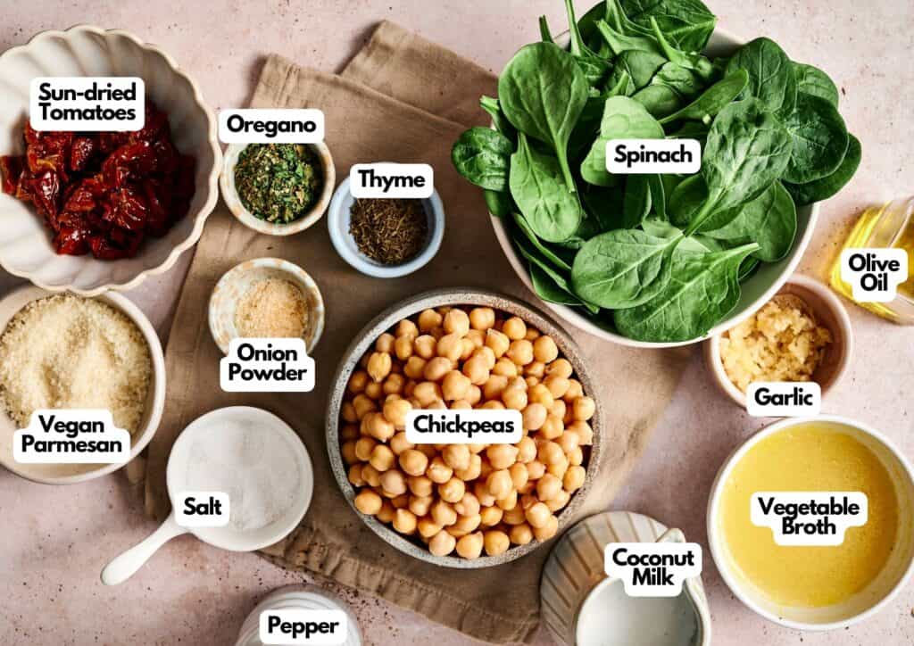 A collection of labeled ingredients on a table, including chickpeas, spinach, coconut milk, sun-dried tomatoes, spices, vegan parmesan, garlic, olive oil, vegetable broth&mdash;perfect for making Air Fryer Marry Me Chickpeas.