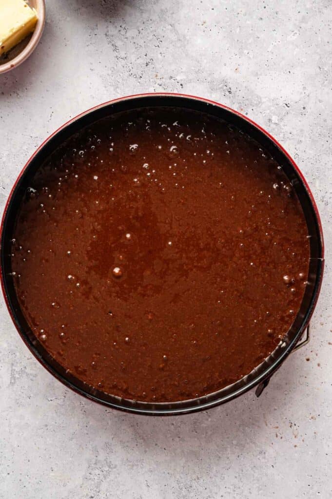 A round cake pan filled with Vegan Chocolate Cake batter sits on a gray countertop.