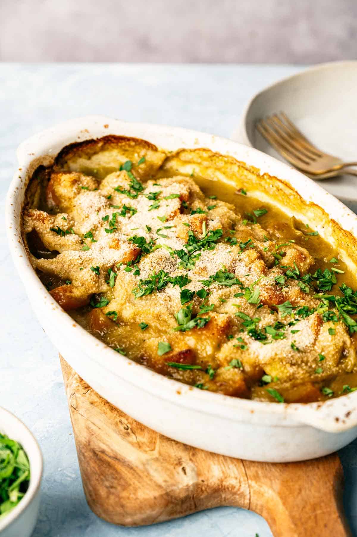 A Vegan Squash Casserole topped with golden bread crumbs and chopped parsley, served in a white oval dish on a wooden board.