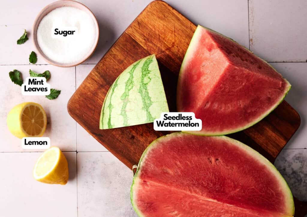 Sliced seedless watermelon on a cutting board with a halved lemon, mint leaves, and a bowl of sugar—perfect ingredients for refreshing Watermelon Sorbet—arranged on a tiled surface.