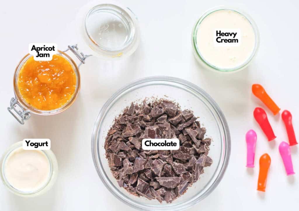 A top-down view of bowls containing apricot jam, yogurt, heavy cream, and chopped chocolate, with colorful deflated balloons beside them&mdash;perfect inspiration for crafting a Vegan Easter Dessert.