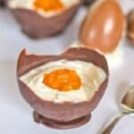 A Vegan Easter Dessert: a chocolate bowl filled with creamy white mousse and topped with an orange jelly resembling an egg yolk, with a spoon and chocolate egg in the background.
