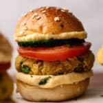 Close-up of Vegan Sliders on a sesame bun with creamy hummus, a juicy tomato slice, crisp cucumber, and a flavorful chickpea patty.
