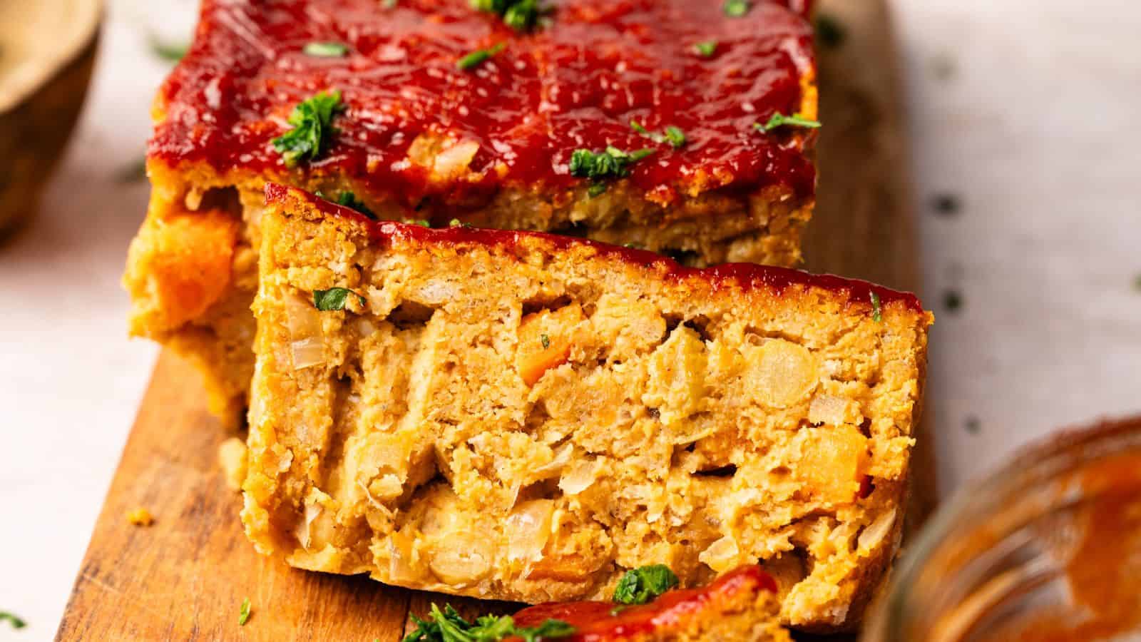 A sliced loaf topped with a red sauce, showing a dense filling of vegetables and legumes, served on a wooden cutting board and garnished with chopped herbs.