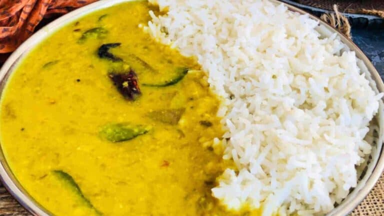 A plate with cooked white rice and yellow dal garnished with green chilies and red chilies.