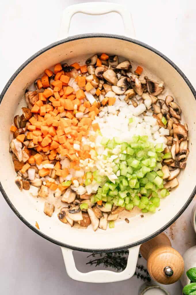 Chopped carrots, onions, celery, and mushrooms arranged in sections in a white pot, ready to be cooked for a delicious Mushroom Bolognese.