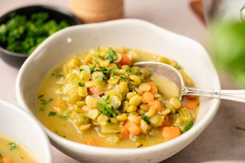 A bowl of hearty Split Pea Soup with diced carrots, celery, and herbs, served with a spoon.