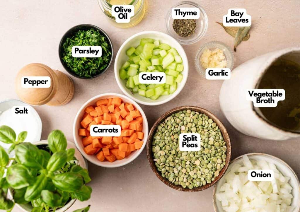 Various soup ingredients for Split Pea Soup, including chopped carrots, celery, onion, parsley, garlic, split peas, vegetable broth, olive oil, thyme, bay leaves, salt, and pepper arranged on a countertop.
