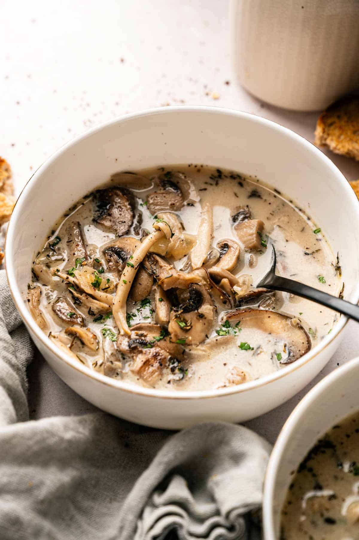 A bowl of creamy Vegan Mushroom Soup with sliced mushrooms and herbs, served with a spoon and garnished with fresh parsley.