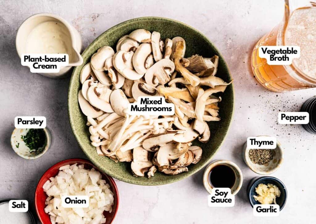A bowl of Vegan Mushroom Soup is surrounded by labeled ingredients: plant-based cream, vegetable broth, parsley, salt, onion, soy sauce, thyme, pepper, and garlic.