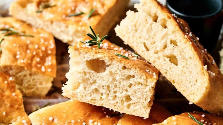 Close-up of sliced focaccia bread topped with coarse salt and rosemary, showing a light, airy crumb.