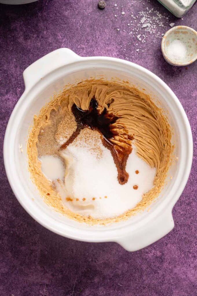 A white mixing bowl contains creamed butter, sugar, and vanilla extract—the perfect base for delicious Peanut Butter Chocolate Chip Cookies—sitting on a purple countertop.