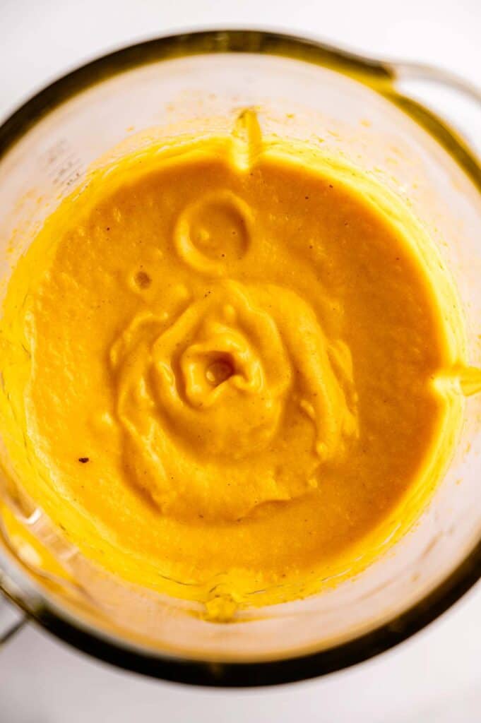 Blended Vegan Carrot Soup with an orange-yellow hue in a glass blender jar, viewed from above on a white background.