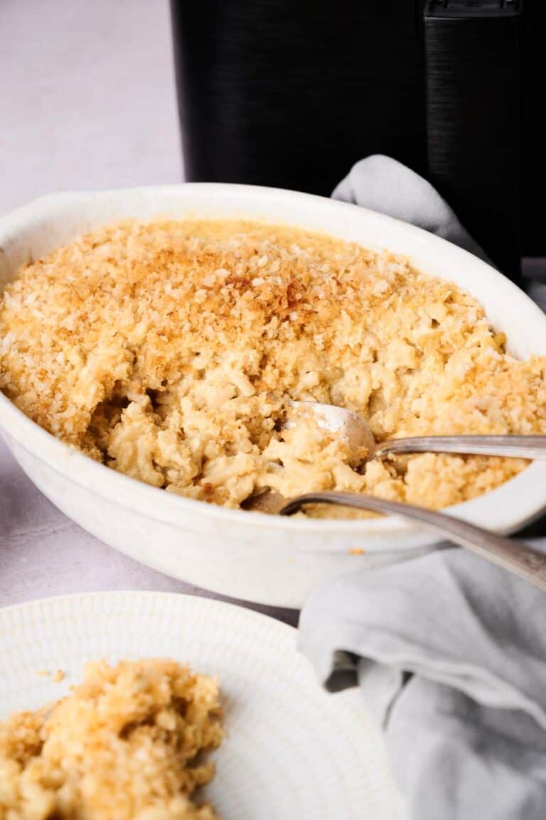 A white baking dish filled with creamy Air Fryer Mac and Cheese, topped with a golden breadcrumb crust, with a serving spoon and fork inside.