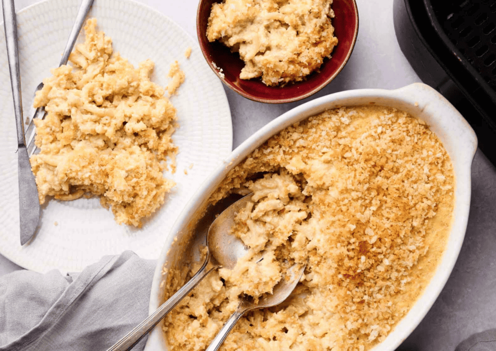 A baked Air Fryer Mac and Cheese casserole with a golden breadcrumb topping, partially served into a bowl and a plate with serving utensils.