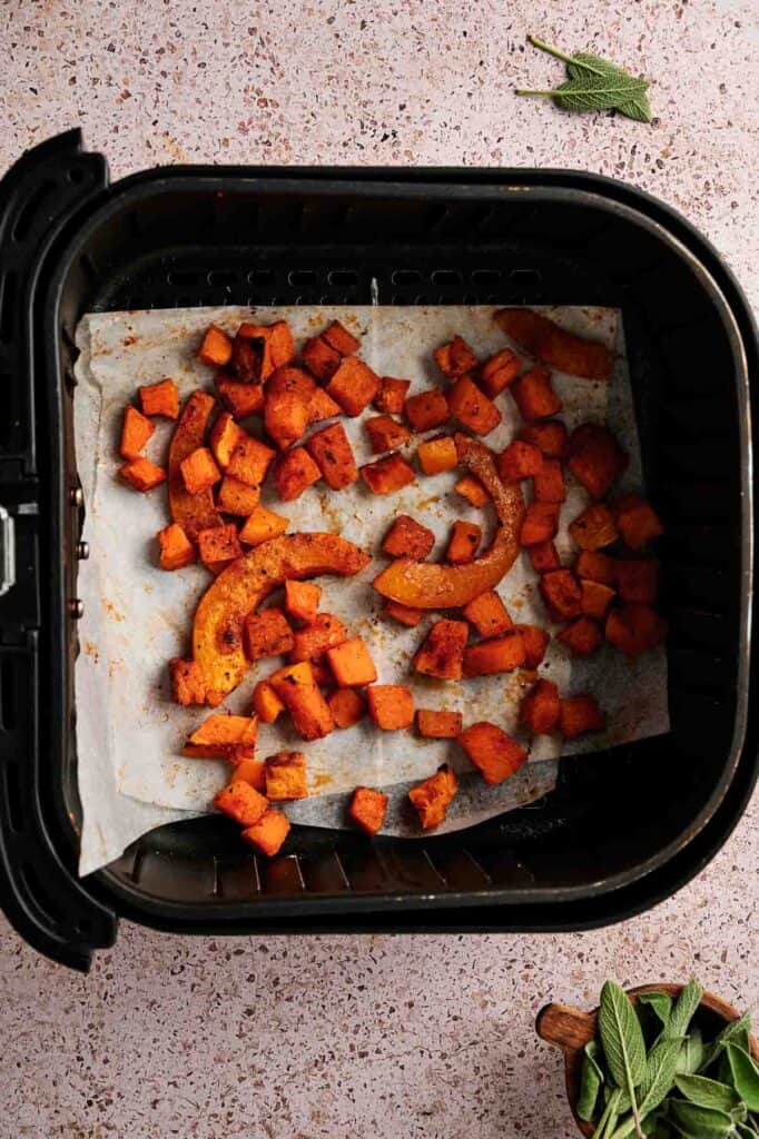 Seasoned pumpkin pieces roasted on parchment paper inside an air fryer basket.