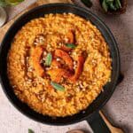 A pan of Air Fryer Pumpkin Risotto garnished with roasted pumpkin slices, chopped nuts, and fresh sage leaves on a light countertop.