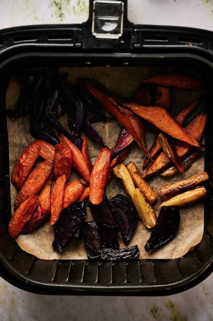 Air Fryer Roasted Root Vegetables&mdash;carrots, beets, and parsnips&mdash;are arranged on parchment paper in the basket, creating a vibrant and healthy side dish with minimal oil.
