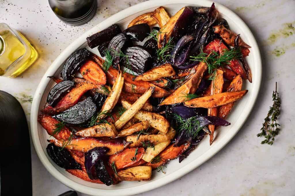 Oval platter of Air Fryer Roasted Root Vegetables, including carrots, parsnips, and red onions, garnished with fresh herbs and black pepper.