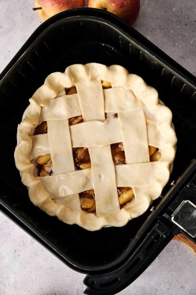 Unbaked Air Fryer Vegan Apple Pie with a lattice top sits in the air fryer basket, ready to be cooked.